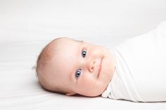 a baby laying on its side wearing a white shirt and looking up at the camera