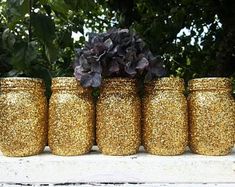 gold glitter jars with flowers in them sitting on a ledge next to some bushes and trees