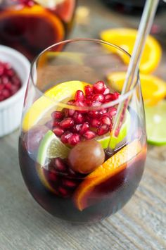 a glass filled with liquid and fruit on top of a wooden table next to other glasses