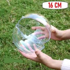 a person holding a clear plastic object in their hand on the grass with one hand reaching for it