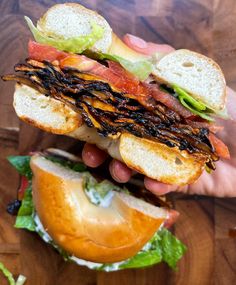 a hand holding a sandwich with meat, cheese and lettuce