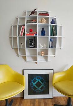 two yellow chairs sitting in front of a white book shelf with books on top of it