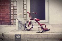 a red tricycle parked next to a fire hydrant on the side of a building