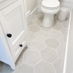 a white toilet sitting inside of a bathroom next to a sink and shower stall with hexagonal tiles on the floor