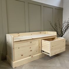 a wooden bench with two drawers on the bottom and an open drawer below it in front of a wall