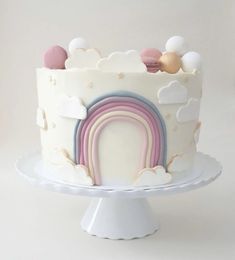 a white cake with rainbows and clouds on top is sitting on a plate in front of a white background