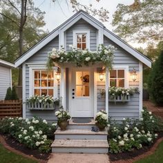 a small gray house with white flowers on the front door and steps leading up to it