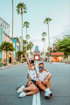 a man and woman sitting on the ground with their arms in the air while wearing masks