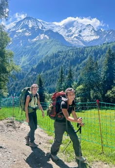 two people with backpacks are walking up a trail in the mountains near a fence