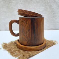 a wooden coffee cup with a lid on a burlly place mat next to a white wall