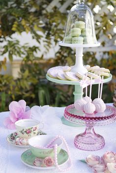 a table topped with plates and cups filled with desserts next to a cake stand