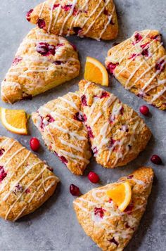 cranberry orange scones with icing on a gray surface next to sliced oranges and cranberries