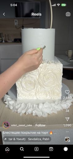 someone is decorating a cake with white icing and flowers on the bottom layer