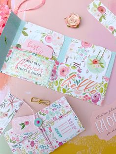 some cards and papers are laying on a table with pink flowers in the background,