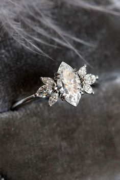 a diamond ring sitting on top of a black velvet cushioned surface, with white feathers in the background