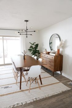 a dining room table with white chairs and a large mirror