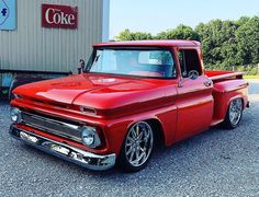 an old red pickup truck parked in front of a coke cola sign on the side of a building