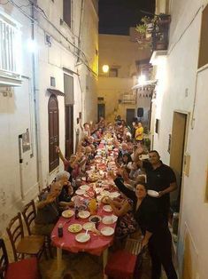 a group of people sitting at a long table with plates on it in an alleyway