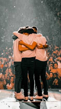 three people hugging each other while standing on a stage with an audience in the background