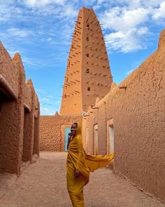 a man in yellow is walking through an adobe - style village with tall buildings on either side