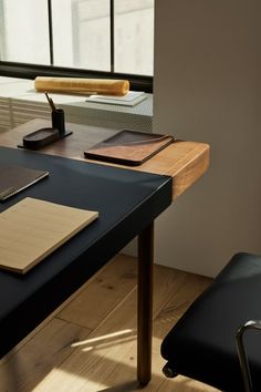 a desk with a pen, notebook and phone on it next to a large window