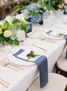 the table is set with white and blue place settings, silverware, and greenery