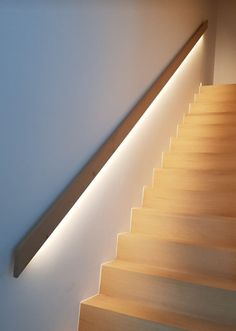 a wooden stair case with lights on the side and below it, along with a white wall