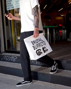 a man holding a shopping bag and cell phone on the side walk in front of a building