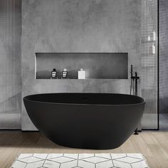 a black bath tub sitting on top of a wooden floor next to a white rug