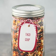 a jar filled with taco soup sitting on top of a counter next to a red and white tag