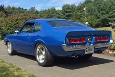 a blue car is parked on the side of the road in front of some bushes