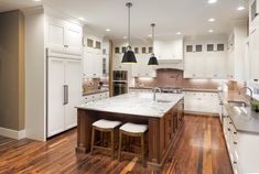 a large kitchen with white cabinets and wooden flooring on the walls, along with two stools at the center island