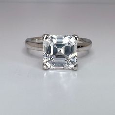 an emerald cut diamond ring on a white surface with the center stone in the middle