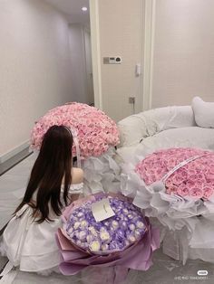 a woman sitting on the floor next to large bouquets of pink and white flowers