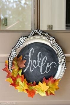 a chalkboard with the word hello painted on it and fall leaves in front of it