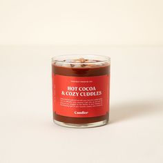 a candle with hot cocoa and cozy cuddles in it on a white surface