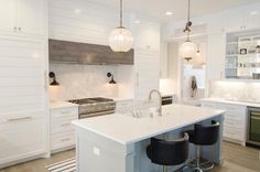 a kitchen with white cabinets and an island in the center, surrounded by black bar stools