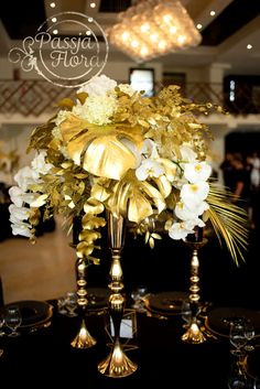 a vase filled with white and gold flowers on top of a black tablecloth covered table