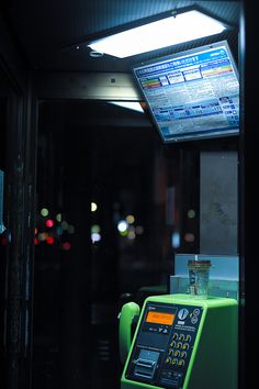 an atm machine sitting on the side of a bus stop at night with lights in the background