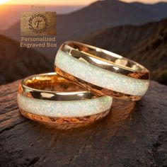 two wedding bands with opalite inlays on top of a rock at sunset