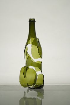 a green glass bottle sitting on top of a reflective table next to a white wall