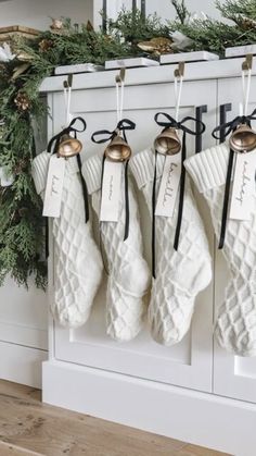 christmas stockings hanging from hooks in front of a mantle with evergreen garland and bells on it