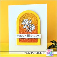 a happy birthday card with an arch and flowers on the front, next to a potted plant