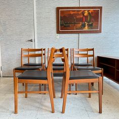 a set of four wooden chairs sitting next to each other in front of a painting