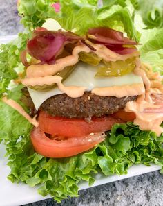 a hamburger with lettuce, tomato and sauce on it sitting on a plate