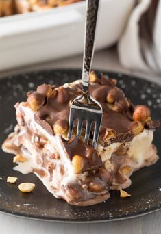 a fork is stuck into a piece of dessert on a plate with nuts and chocolate