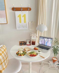 a laptop computer sitting on top of a white table next to a plate of food