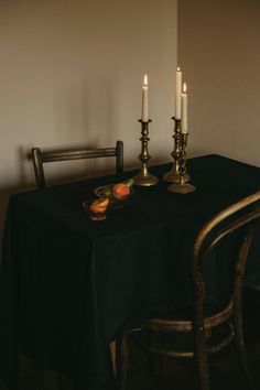 two candles are lit at the end of a dinner table with black cloth on it