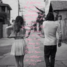 a man and woman walking down the street with pink writing on their back's wall