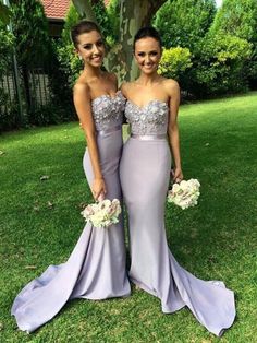 two women standing next to each other in purple dresses and holding bouquets on the grass